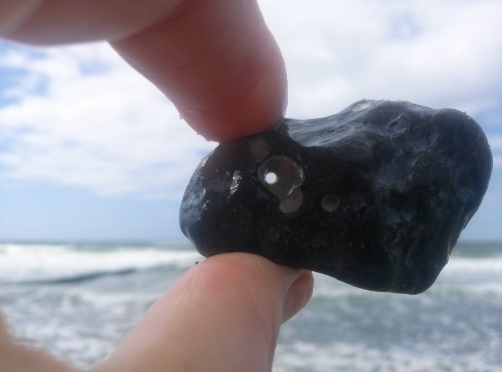 Stein mit Loch in der Mitte, gehalten in den Fingern (Hühnergott)
